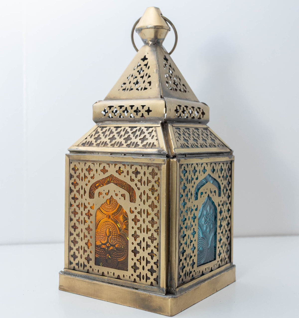Decorative brass-tone lantern with blue and amber glass panels and intricate pierced metalwork, individually selected in Rabat, Morocco.