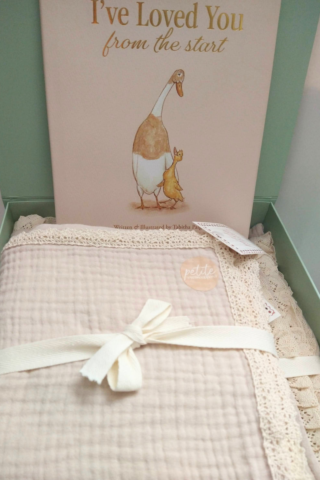 Petite Evelina muslin baby blanket and swaddle shown with keepsake book.