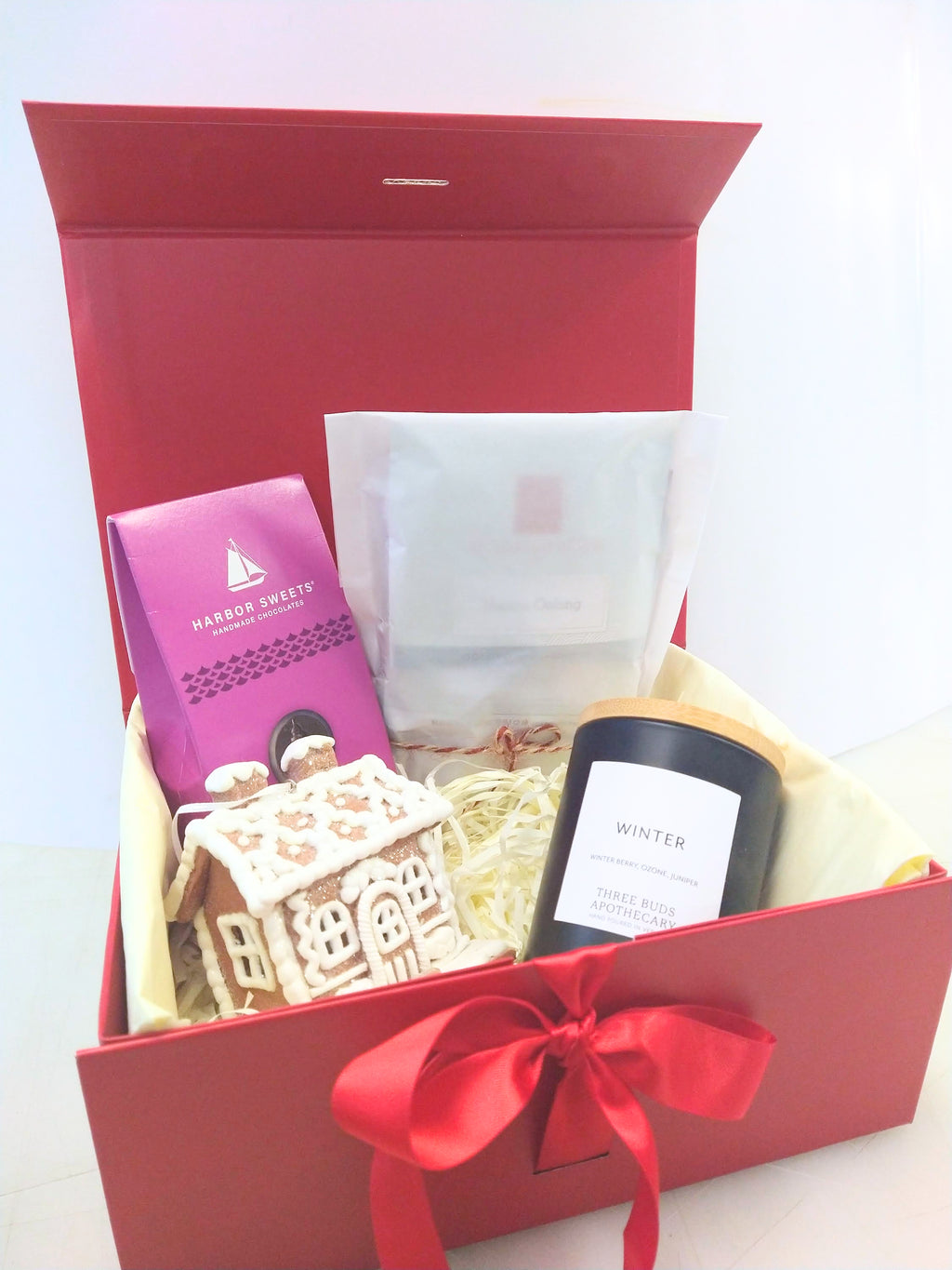Christmas gift box with Vermont Winter candle, Harbor Sweets chocolates, assorted tea and gingerbread house decoration in a red gift box.