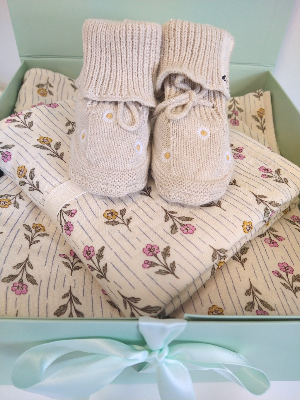 Close up of Petite Evelina Meadow Whisper baby blanket and swaddle with Saga Copenhagen Daisy booties.