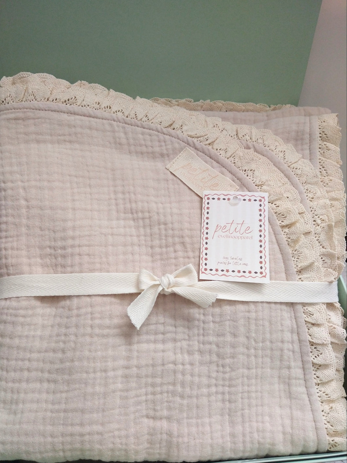 Petite Evelina light beige muslin baby blanket with lace shown inside green gift box.