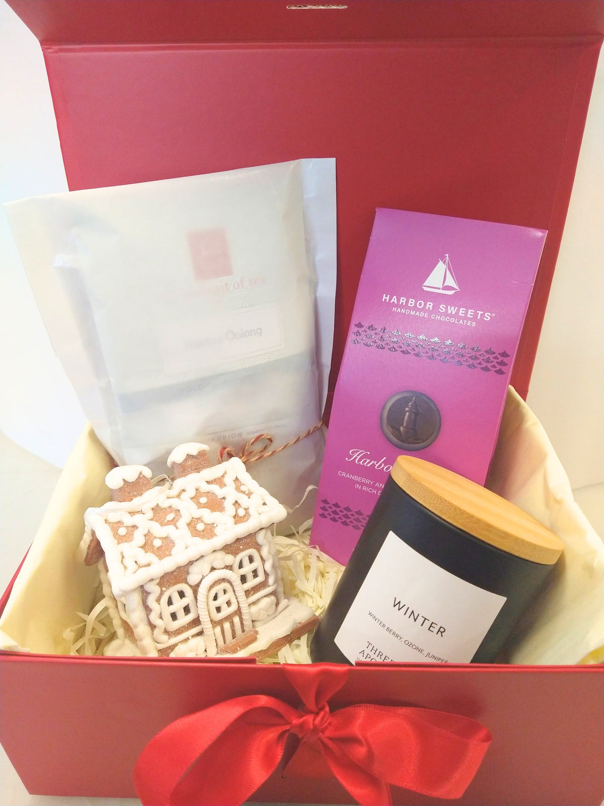 Christmas gift box with Vermont Winter candle, Harbor Sweets chocolates, assorted tea and gingerbread house decoration in a red gift box.