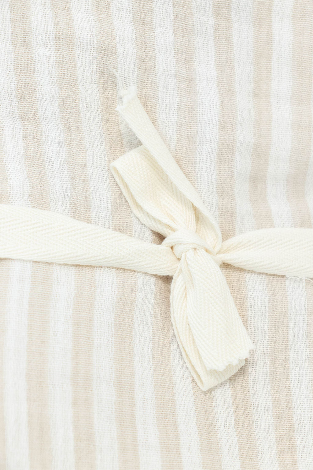 Close-up of Petite Evelina beige striped muslin swaddle with cream cotton tie