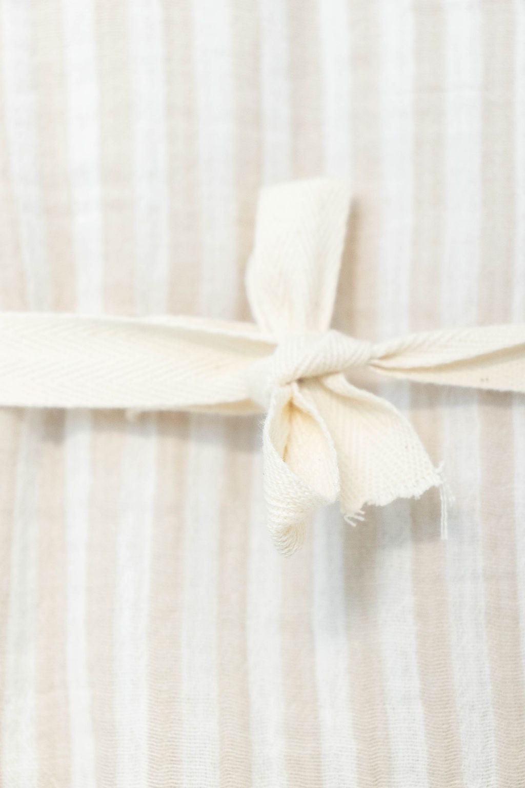 Close-up of Petite Evelina beige striped baby blanket with cream cotton ribbon tie
