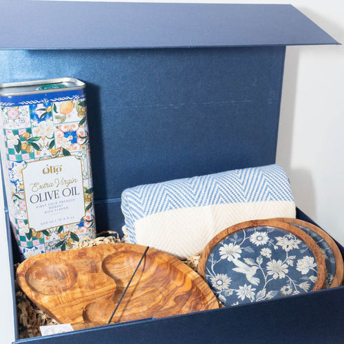 Mediterranean gift box with extra virgin olive oil, two-compartment olive wood serving dish, blue patterned coasters and blue peshtemal towel.
