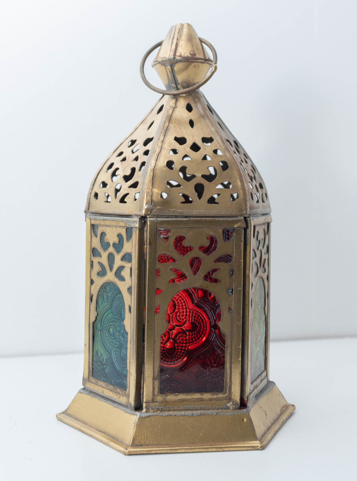Decorative brass-tone lantern with blue and ruby glass panels and intricate pierced metalwork, individually selected in Rabat, Morocco.