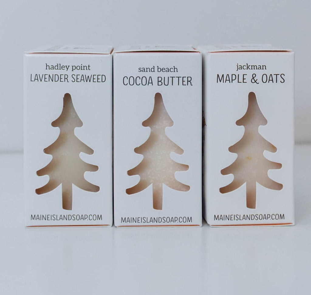 Side view of three Maine Island Soap bars in Lavender Seaweed, Cocoa Butter, and Maple & Oats, featuring tree-shaped package cutouts.