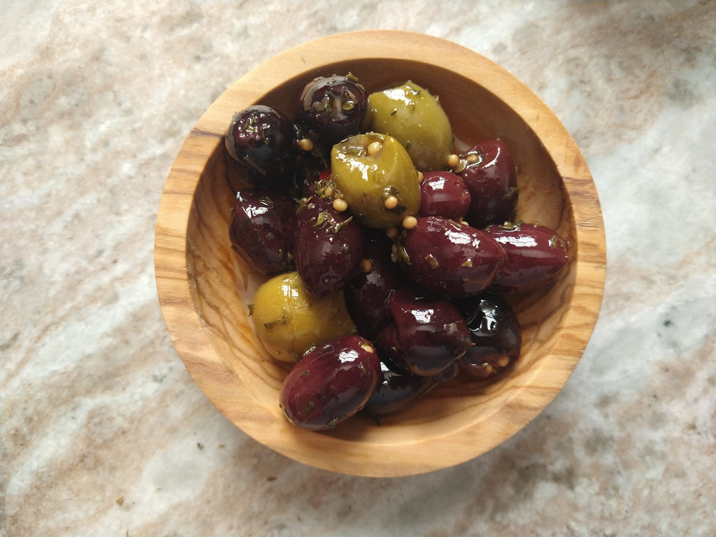 Mixed green and Kalamata olives seasoned with herbs and spices, served in a small olive wood bowl.