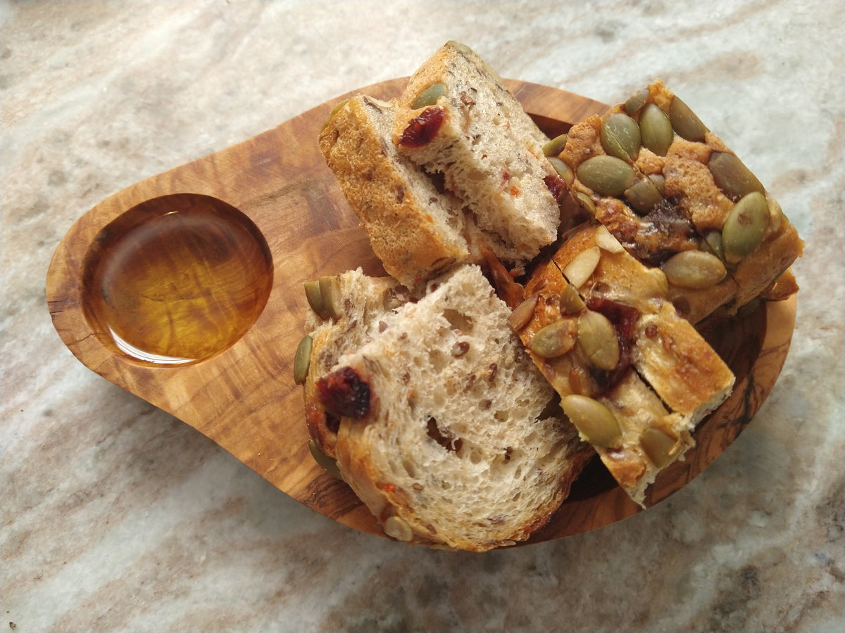 Olive wood serving dish with sliced artisan bread and olive oil.