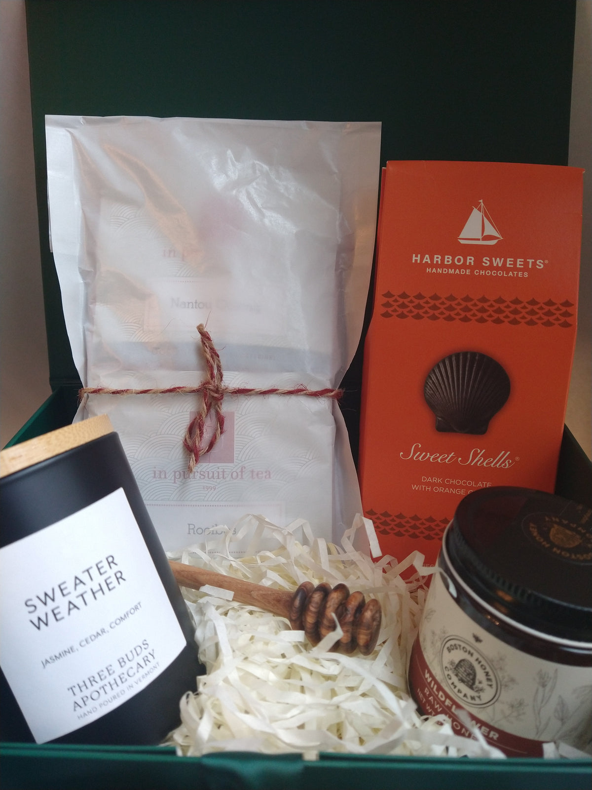 Autumn Gift Box in an open forest-green gift box with satin ribbon, featuring a Three Buds Sweater Weather candle, In Pursuit of Tea assortment, Harbor Sweets chocolates, Boston Honey Company wildflower honey, and an olive wood honey dipper.