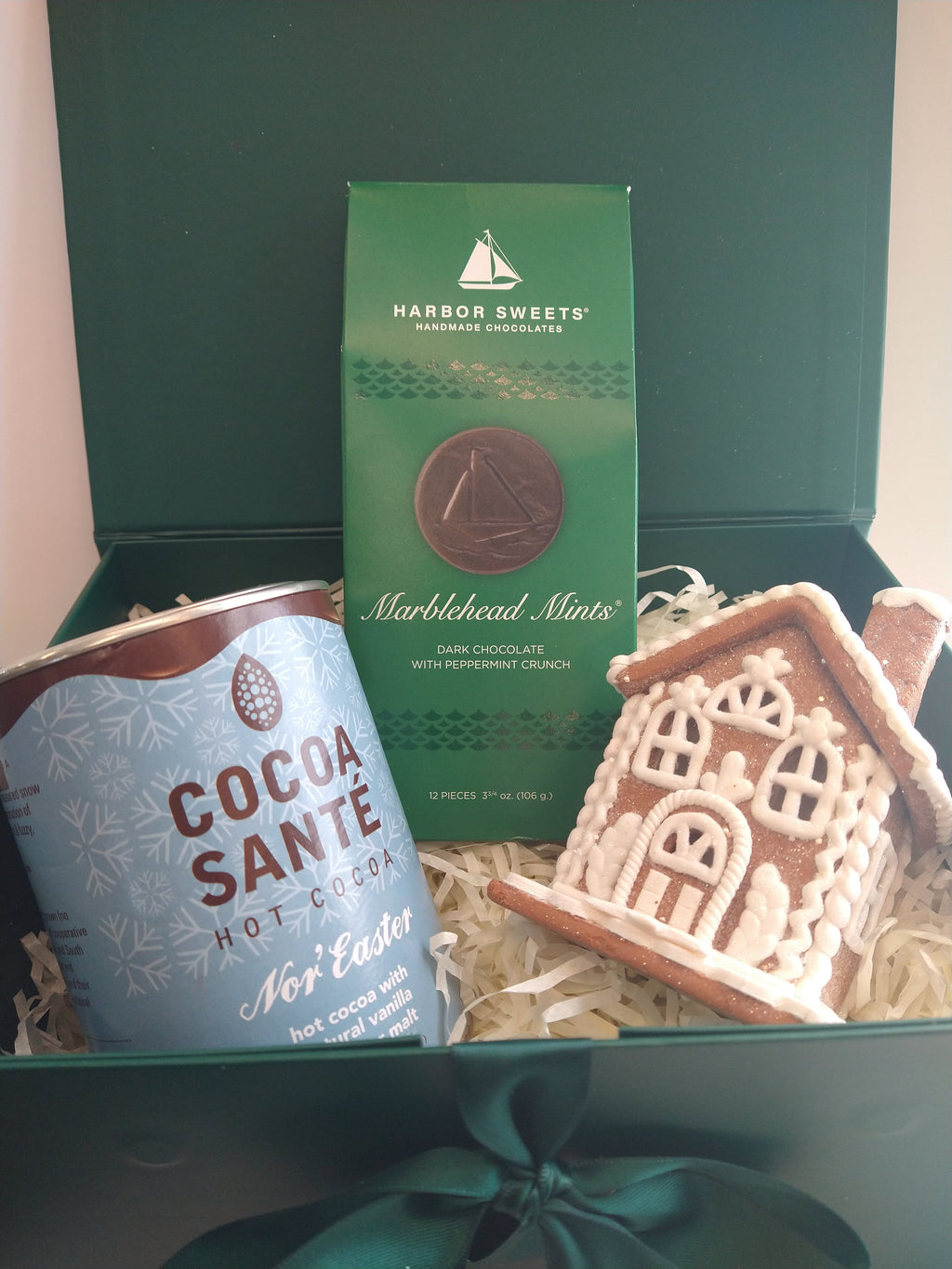 Christmas gift box featuring Cocoa Santé Nor'Easter hot cocoa, Harbor Sweets Marblehead Mints dark chocolates, and a decorative gingerbread house ornament, arranged in an elegant green gift box with ribbon.