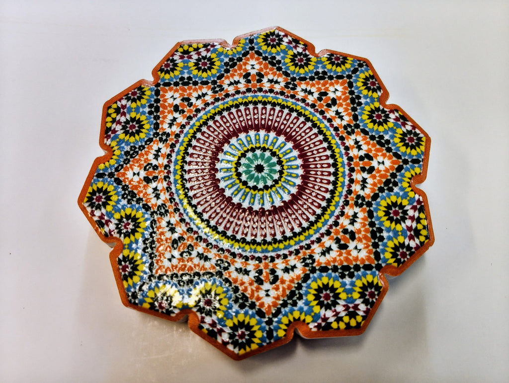 Moroccan-inspired ceramic coaster with a scalloped edge and intricate circular mosaic pattern in burgundy, blue, orange, yellow, green and black.