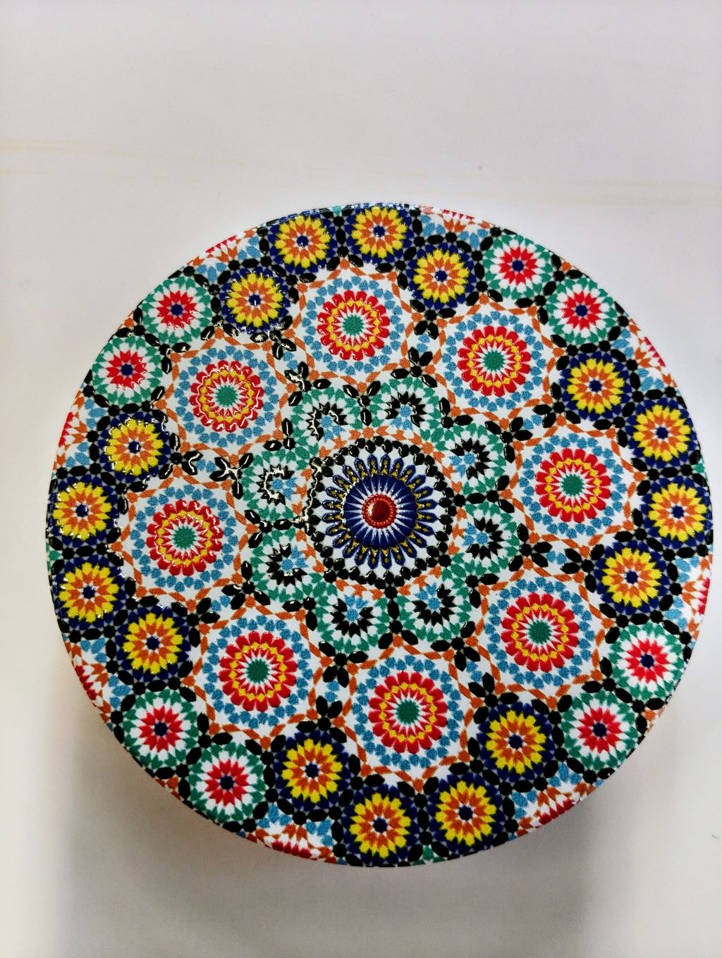 Round Moroccan-inspired ceramic coaster decorated with repeating floral mosaic patterns in turquoise, cobalt blue, orange, yellow, red and white, with a central circular medallion.