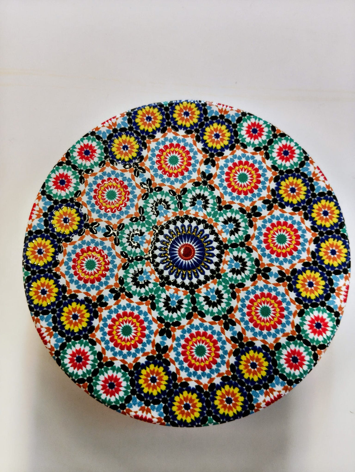 Round Moroccan-inspired ceramic coaster decorated with repeating floral mosaic patterns in turquoise, cobalt blue, orange, yellow, red and white, with a central circular medallion.
