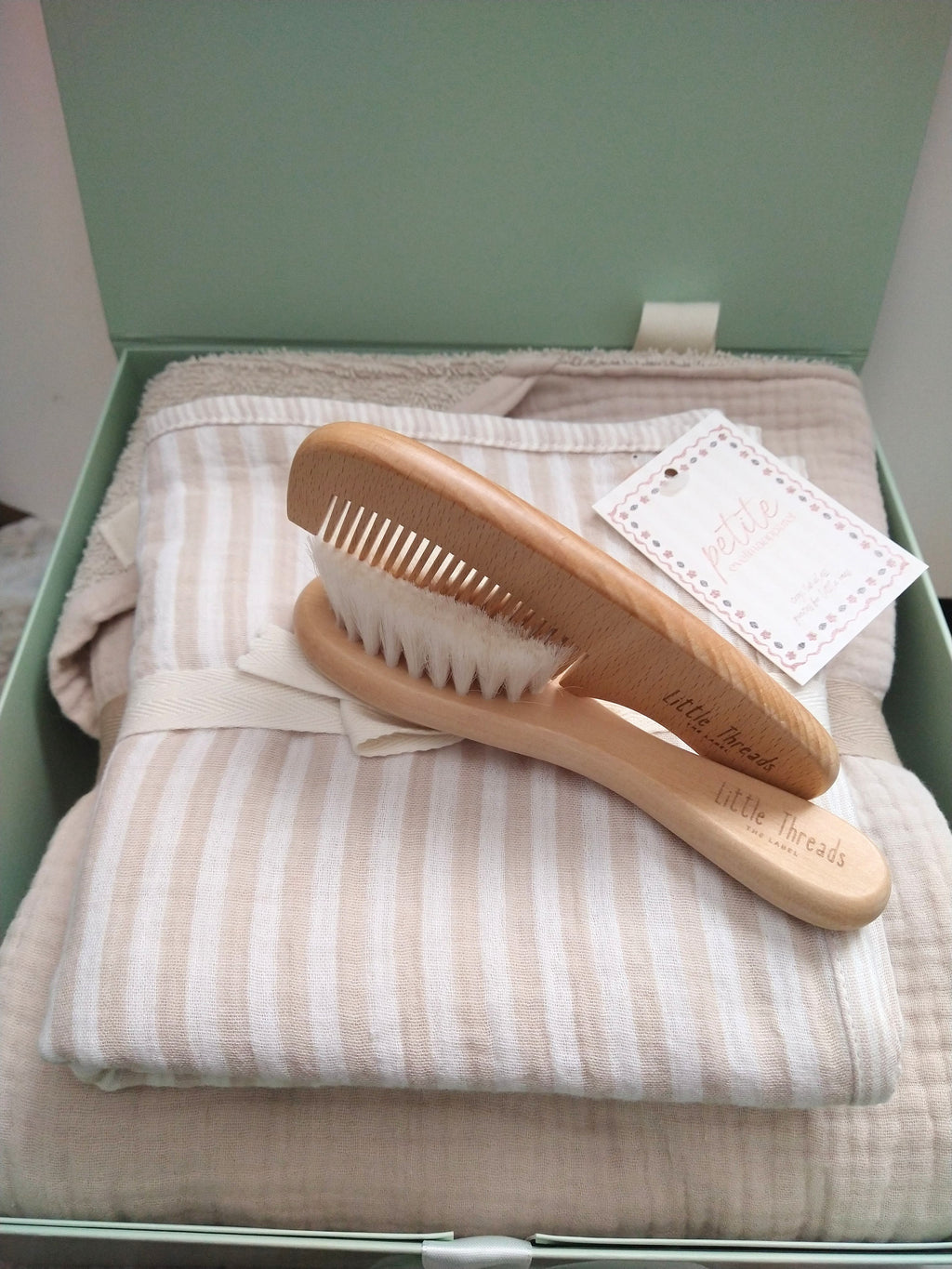 etite Evelina Light Beige hooded towel, Beige Stripes swaddle and Little Threads wooden brush and comb displayed on sage green gift box with coordinating ribbon.