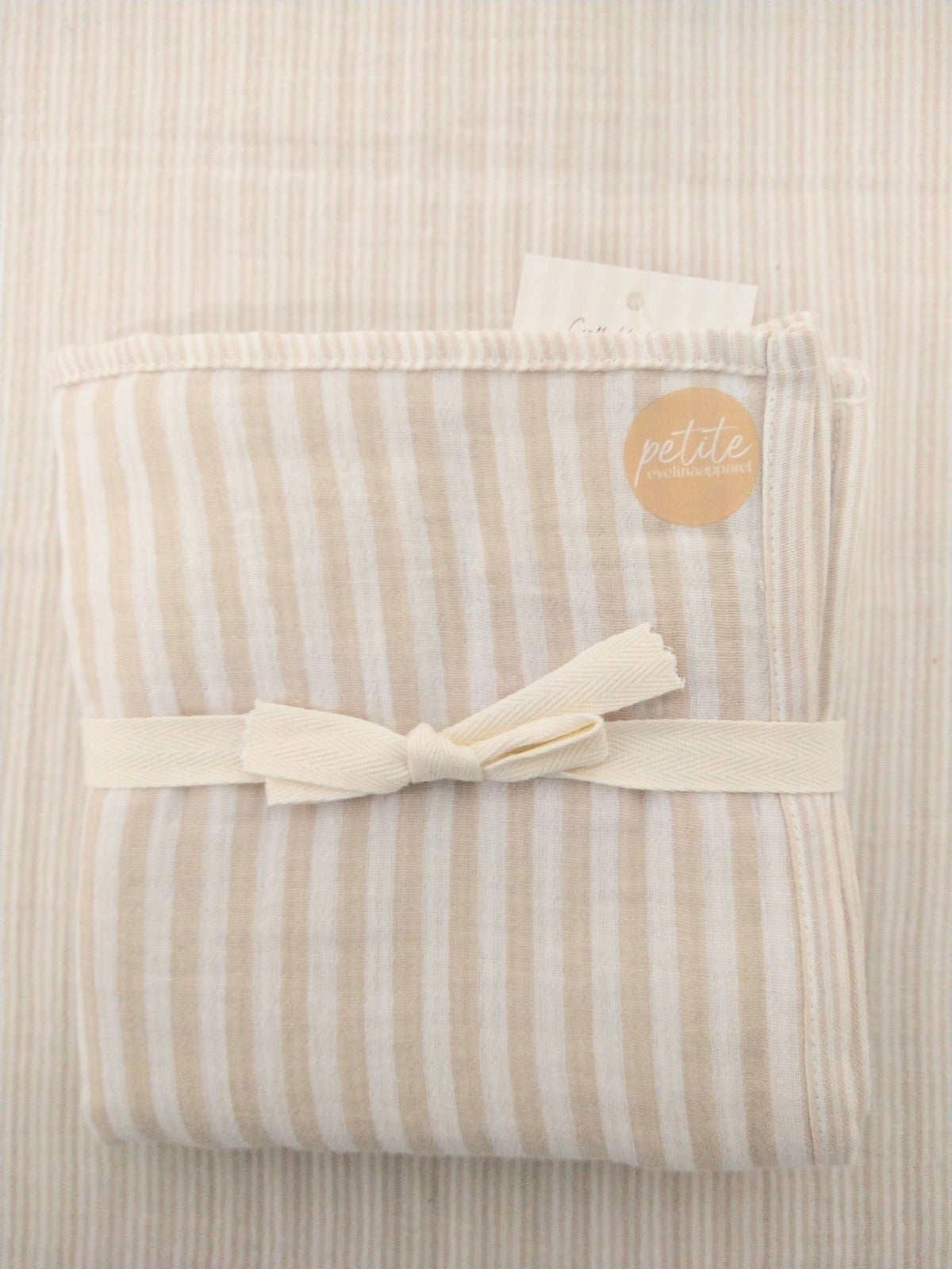 Petite Evelina beige striped muslin swaddle folded and tied over the opened swaddle fabric